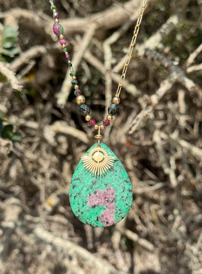 Vert, rose, or - des couleurs qui claquent et vibrent. Une pièce pleine d’énergie et de style.

Collier sur chaîne maille rectangle en or laminé - Pendentif "goutte" de 6 cm en rubis zoïsite et breloque rayon de soleil en or laminé - Perles de rubis zoïsite et en or laminé 14 carats.
